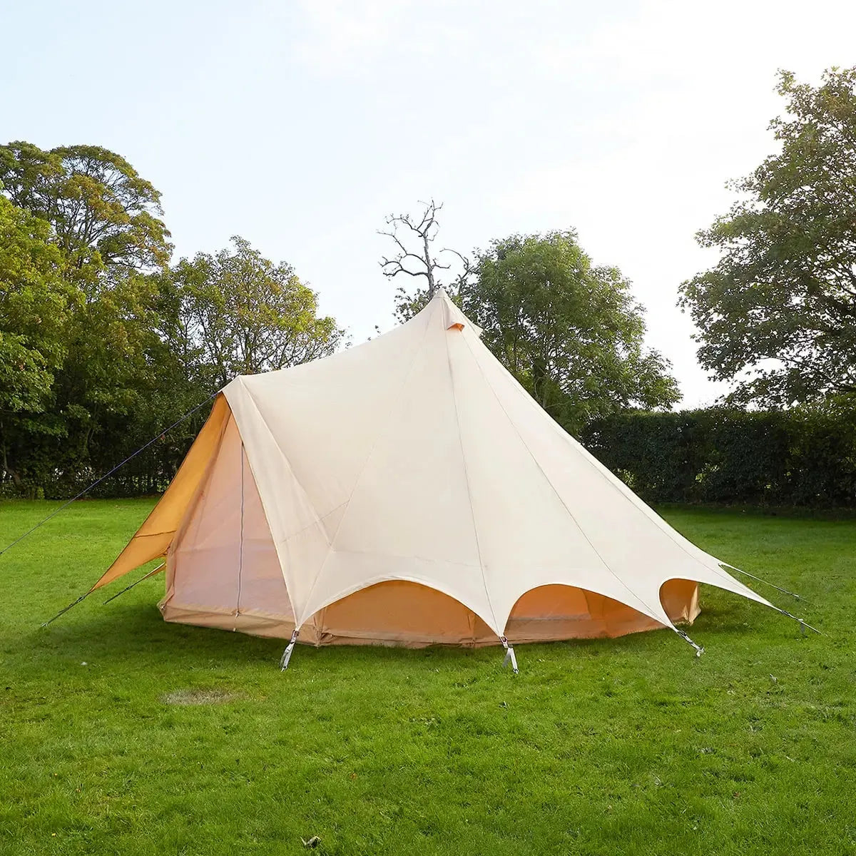 Beige bell tent on grass with trees in the background