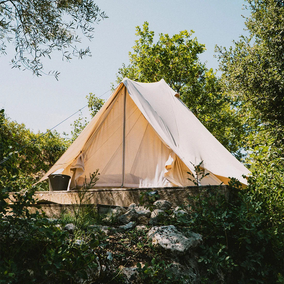 boutique camping bell tent plus 4m tent with netting door closed and trees and plants in the foreground and background