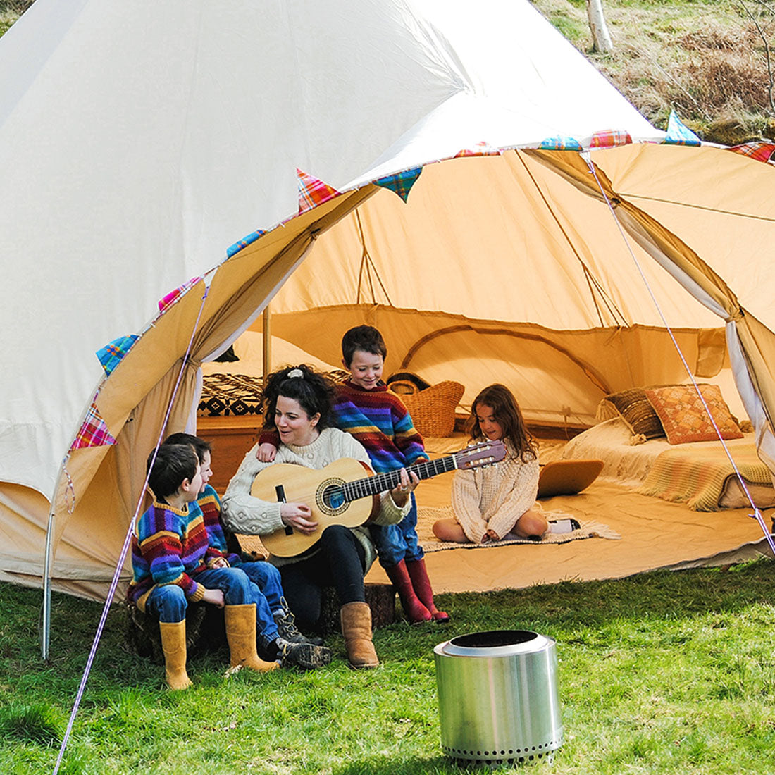 a woman and her family enjoying camping with a guitar and fire outside a 6m star bell tent