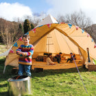 a sunny field with a star bell tent and a boy outside infront of a fire