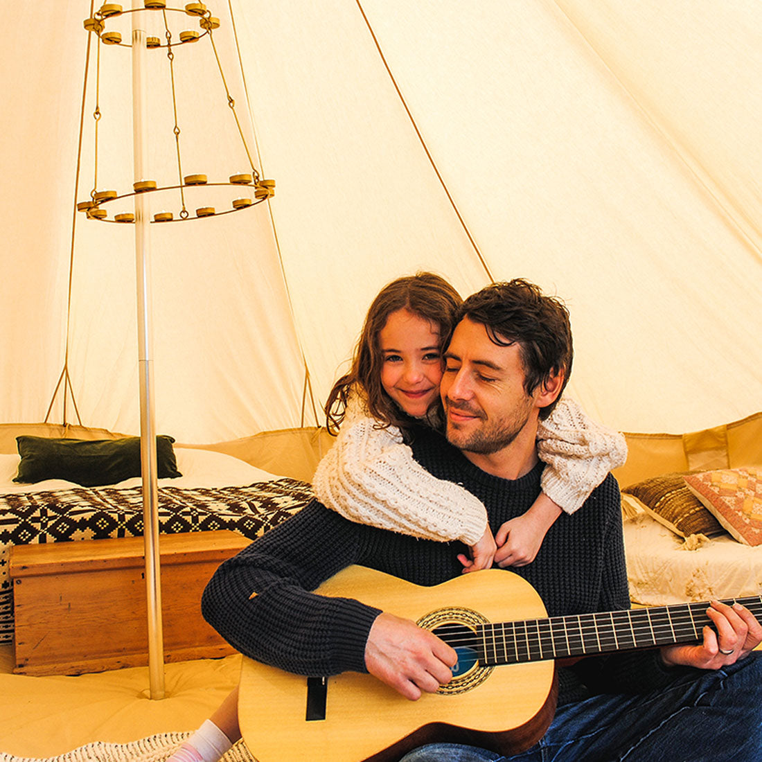 a girl hugging her dad who is holding a guitar inside a boutique camping 6m tent
