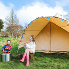 a girl and a boy sitting on logs toasting and eating marshmallows outside a sandstone star bell tent in a green field