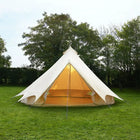 Bell tent with glowing interior on a grassy field with trees in the background