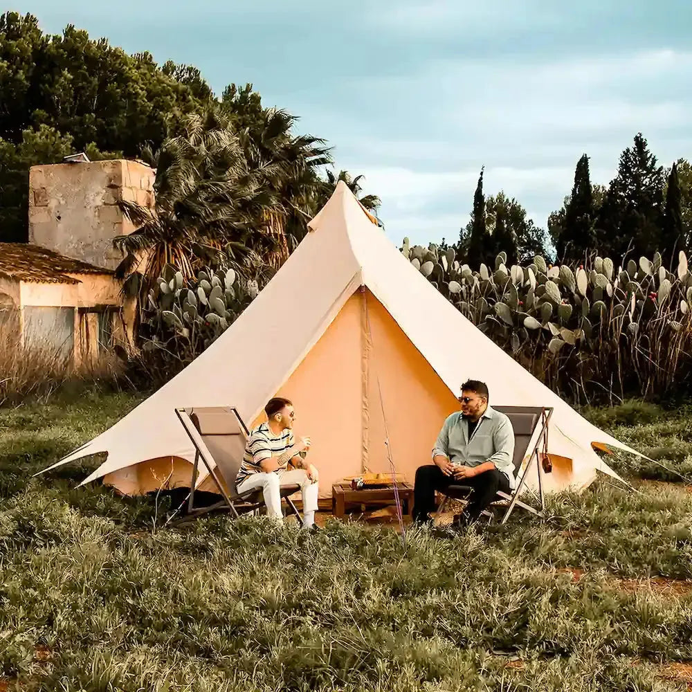 Two people sitting in front of the Bell Tent Plus in a natural setting with trees and plants.