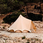 Beige bell tent set up in a natural outdoor setting with rocks and greenery.