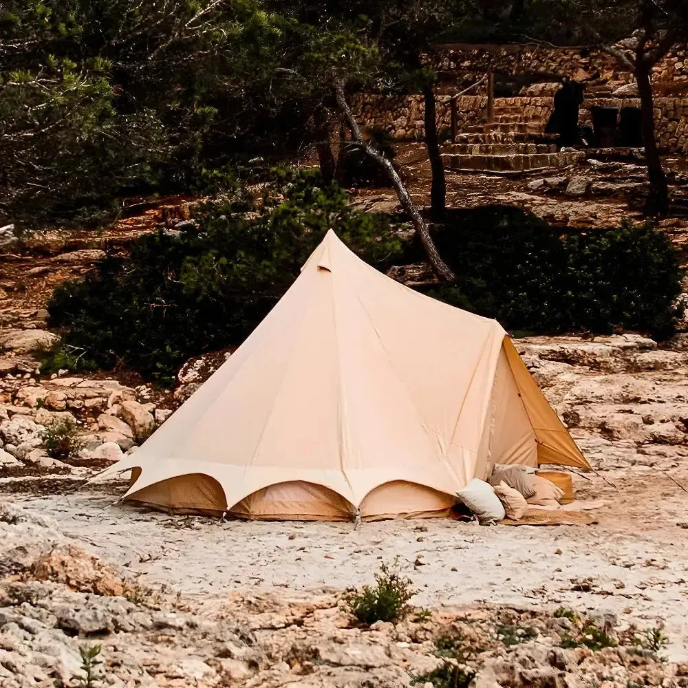 Beige bell tent set up in a natural outdoor setting with rocks and greenery.
