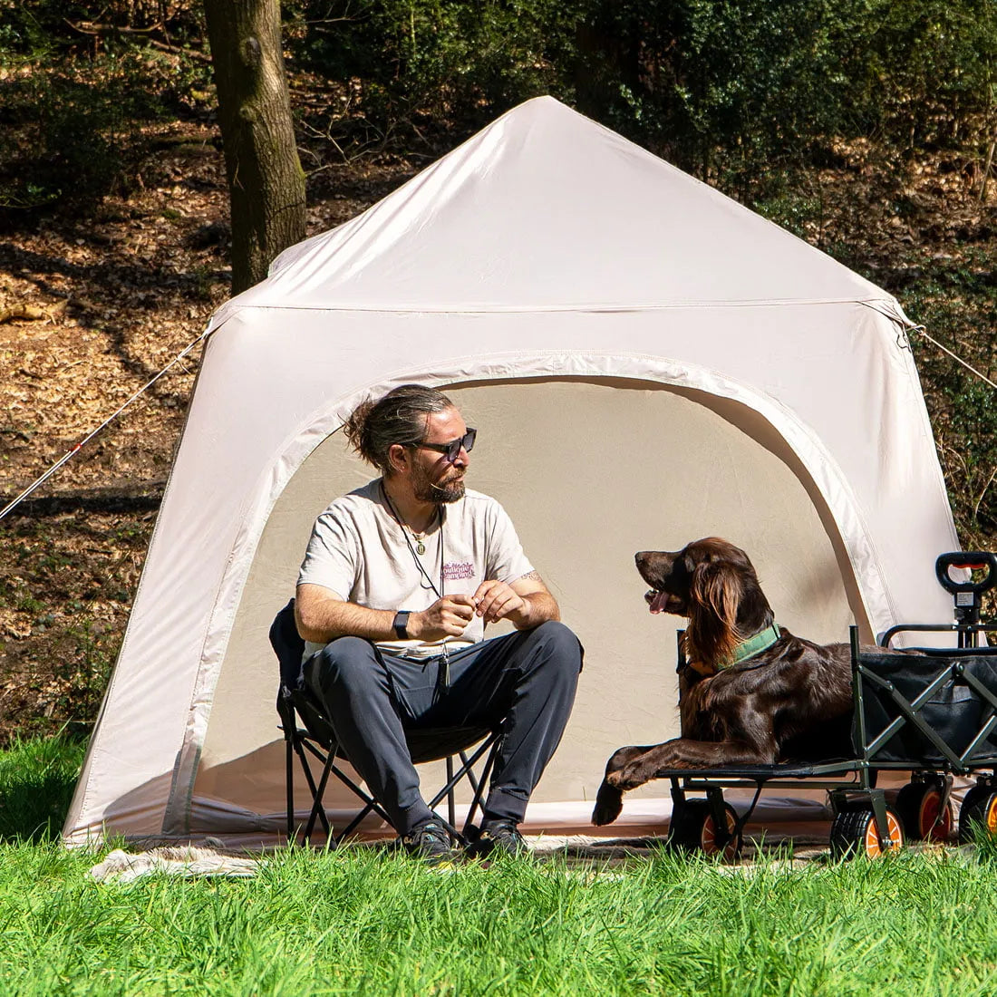 man and dog sitting outside boutique camping tent, the dog is sitting in a boutique camping trolley