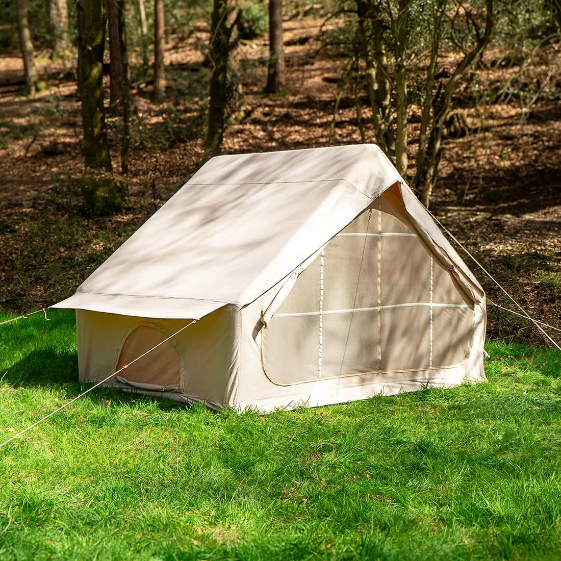 Vela Air Tent set up alone on a grassy field surrounded by trees, in bright natural light.