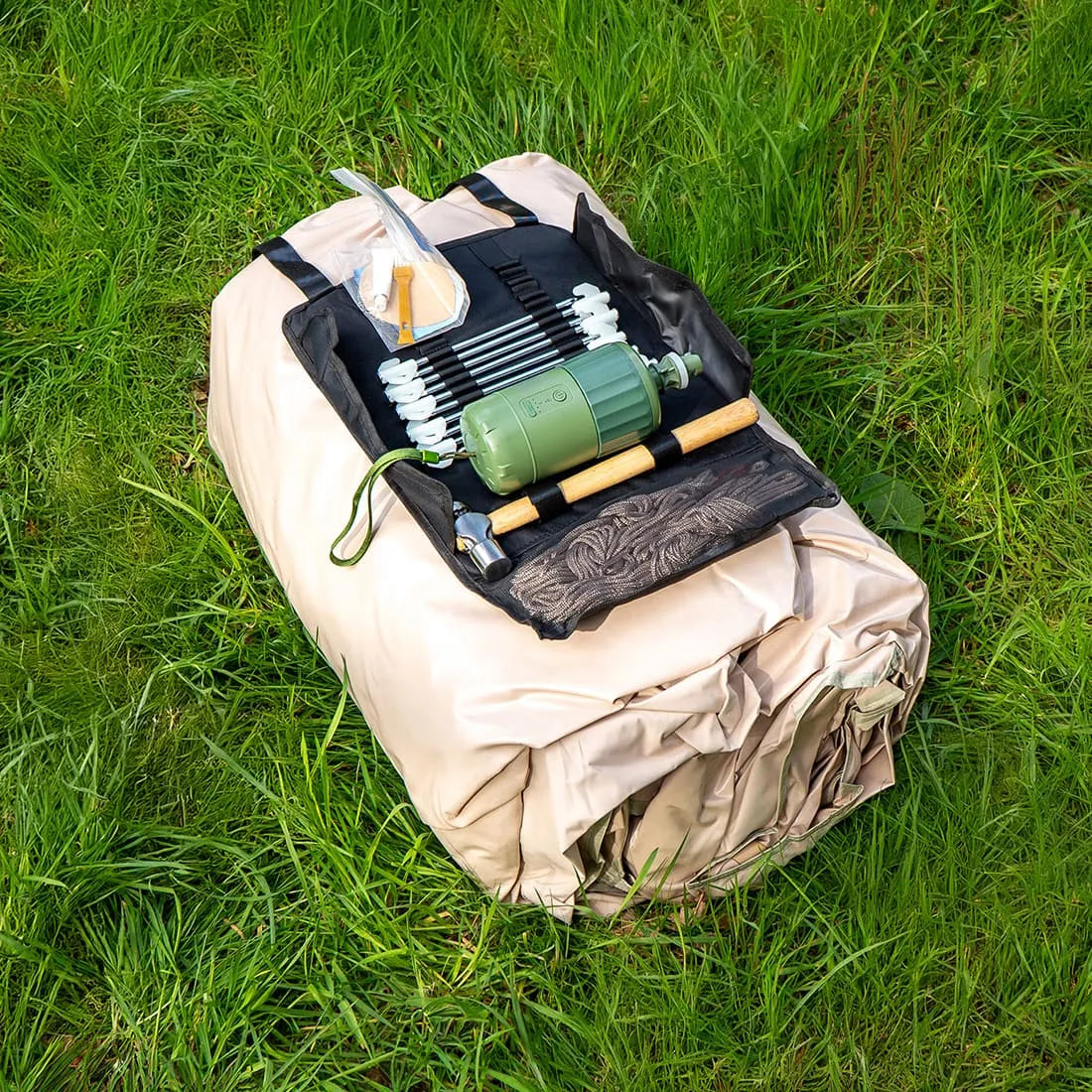 Vela Air Tent packed tightly in a beige carry bag with an air pump placed on top, set on green grass.