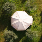 An overhead aerial view of a boutique camping nova air dome glamping tent pitched on green grass among trees.