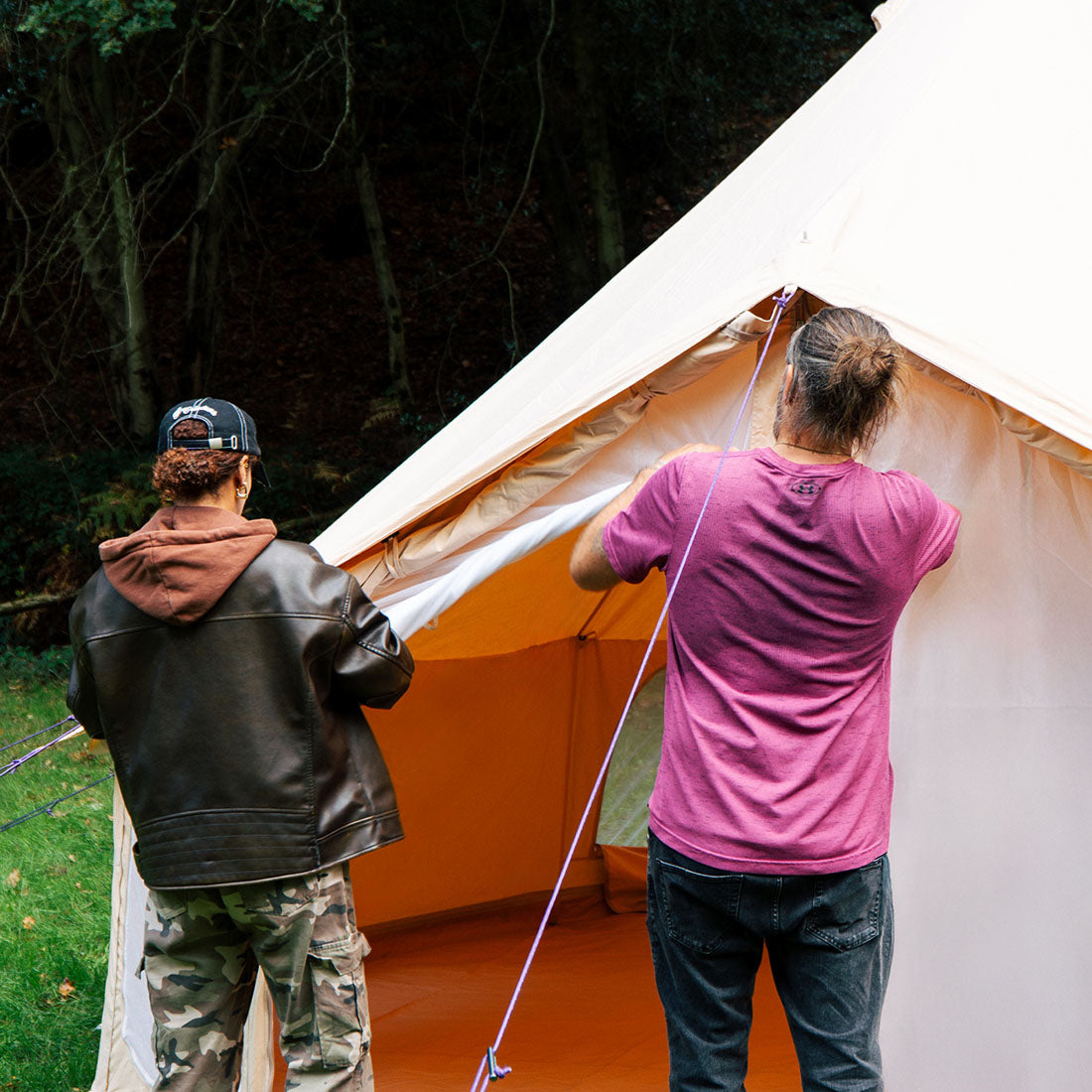 Two people setting up a Bell Tent Pro tent outdoors with trees in the background