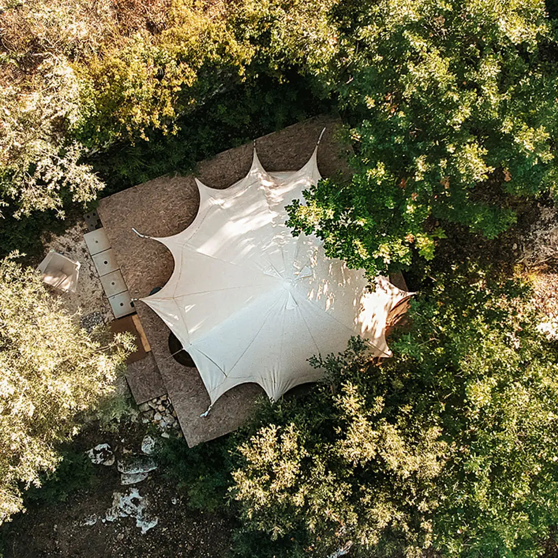boutique camping bell tent plus aerial view on a platform within a group of trees in the sun 