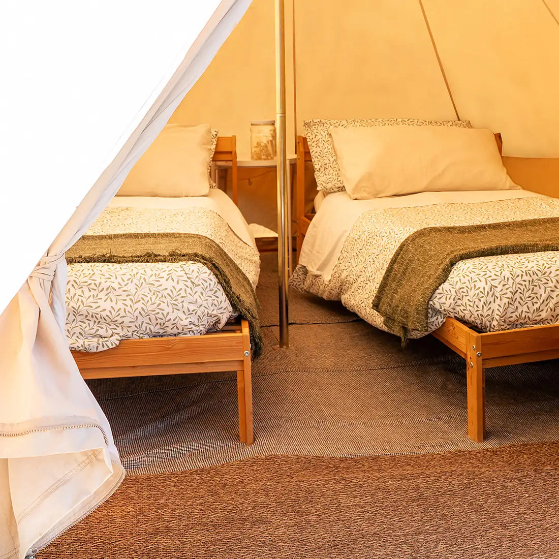 Two wooden beds inside a boutique camping bell tent plus glamping tent with patterned bedding and pillows.