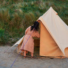 Person in a striped dress standing next to a boutique camping bell tent plus glamping tent on a sandy beach.