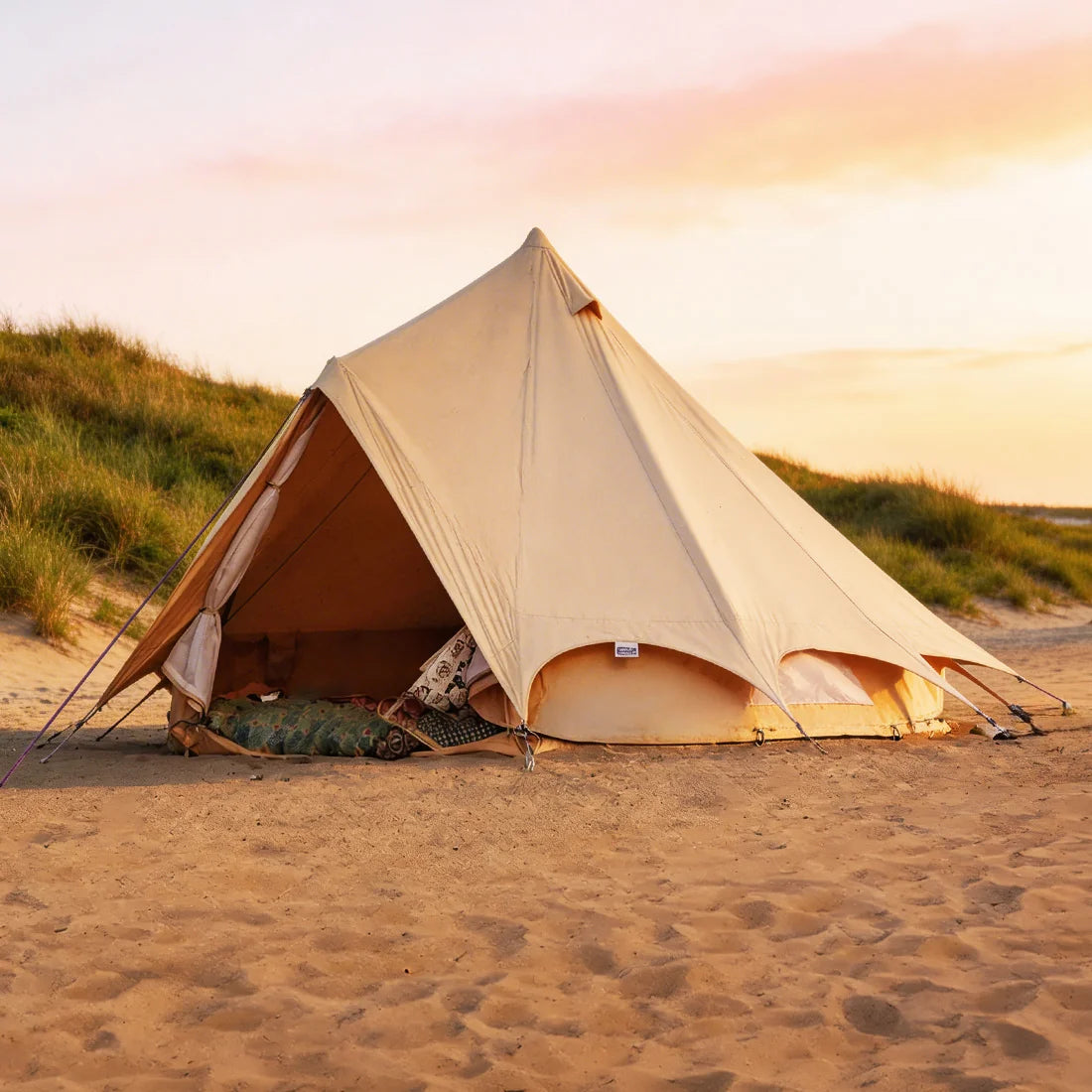 bell tent plus on a sandy beach with a sunset in the background