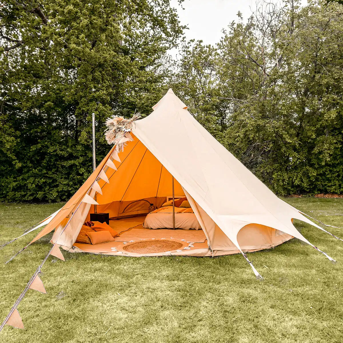 Bell tent plus with interior bedding on a grassy area with trees in the background