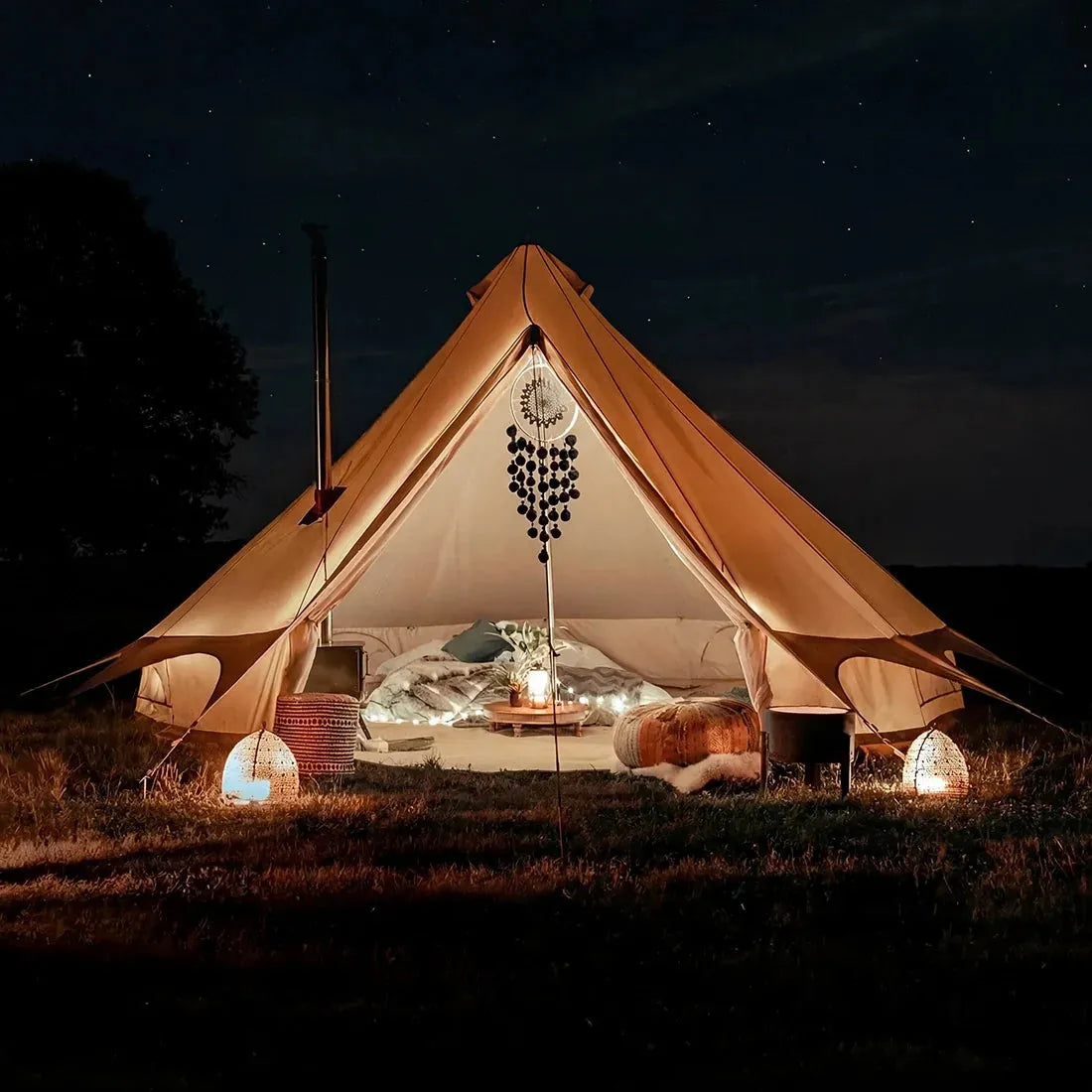 Lit bell tent plus in a field at night with decorative lights and pillows.