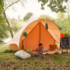little boy playing outside of boutique camping star bell tent reading a book by a lake