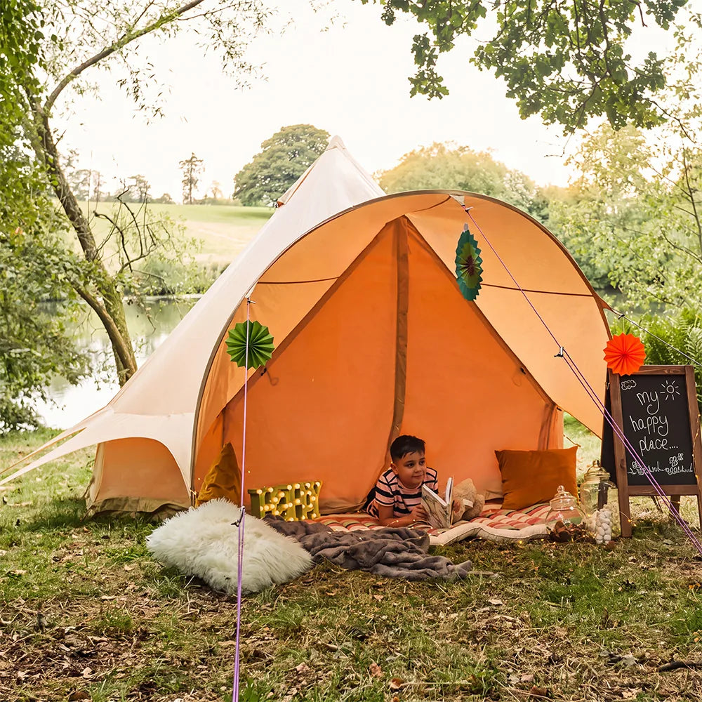 little boy playing outside of boutique camping star bell tent reading a book by a lake