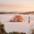 boutique camping star bell tent pitched on sand with man at golden hour walking towards tent