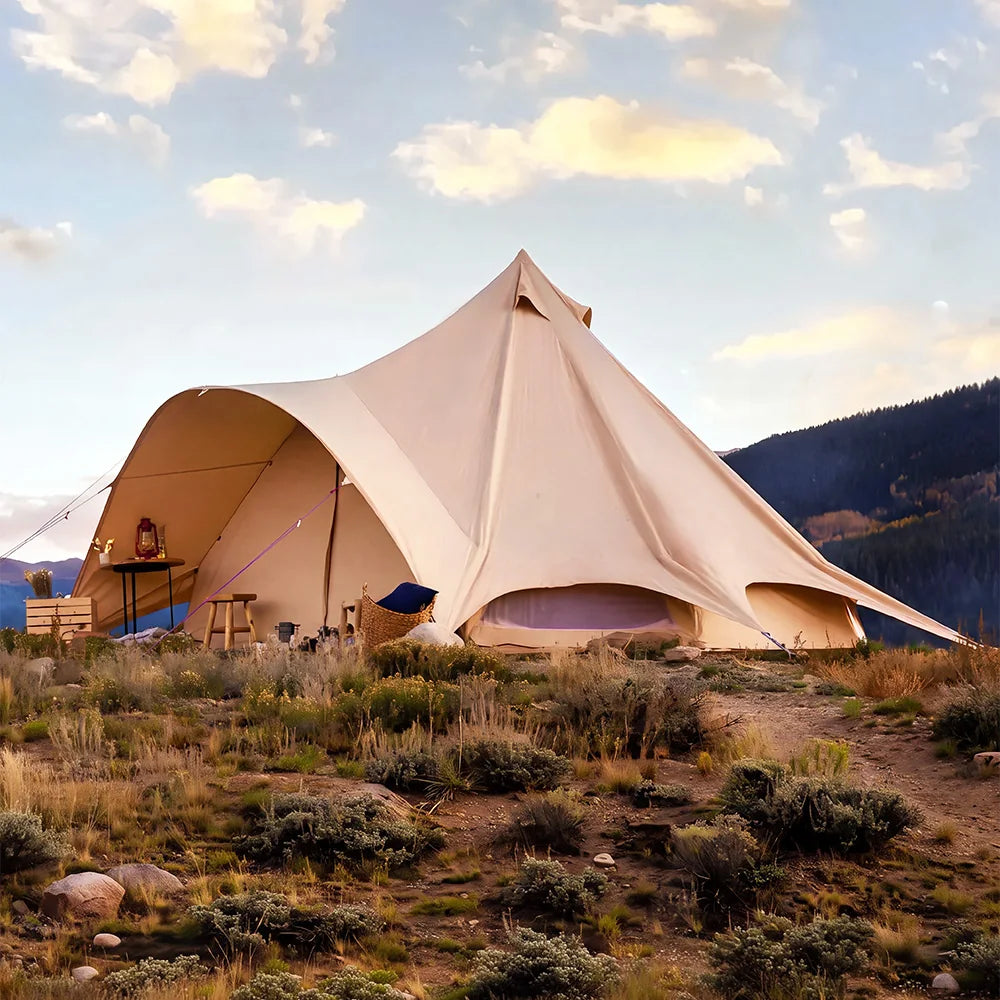 boutique camping star bell tent pitched on grassy hill with mountains in back