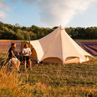 two men outside boutique camping star bell tent in lavender field on bikes enjoying a bottle of beer
