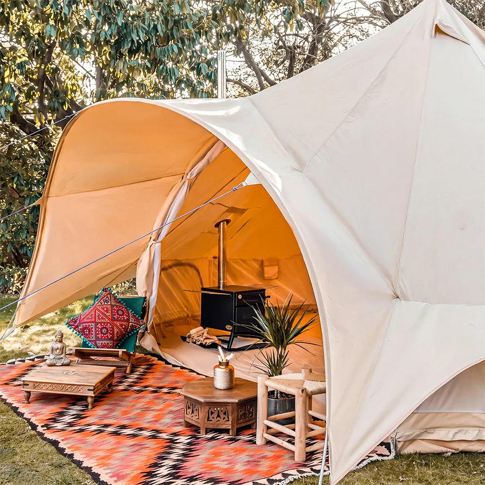 boutique camping star bell tent pitched on grass with stove inside and rugs