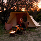 woman sitting by a campfire in front of a tucana double door tent with a sunset in the background 