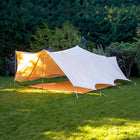 tucana double door bell tent with sides up with orange sunset glow set up in a grassy area with trees in the background
