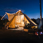 tucana tent glowing with string lights and cosy glamping atmosphere with a stove outside and night sky in a natural setting 