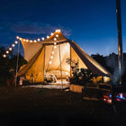 tucana tent glowing with string lights and cosy glamping atmosphere with a stove outside and night sky in a natural setting 