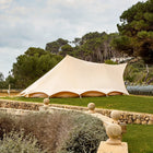 sandstone tucana tent side view set up in a large garden with trees and stone wall in the background 