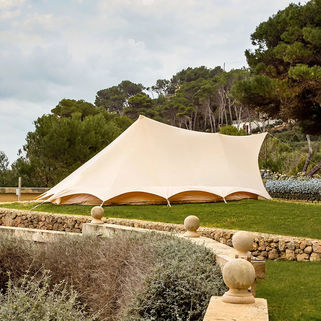 sandstone tucana tent side view set up in a large garden with trees and stone wall in the background 
