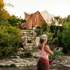 woman doing yoga standing in a natural setting with greenery and a stone staircase leading to a boutique camping tucana bell tent 