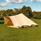 boutique camping tucana bell tent side view set up in a grassy field with trees in the background and blue skies