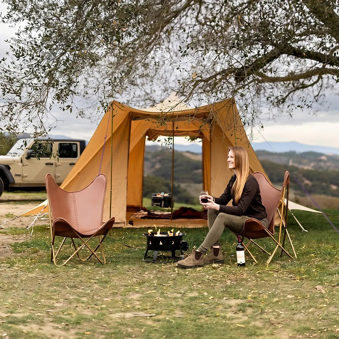 Woman sitting in a chair near a boutique camping tucana tent with a scenic view in the background

