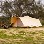Person sitting near a boutique camping tucana double door tent in a natural setting with trees and grass.