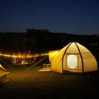 nightime shot of the nova air dome tent in a field with a family surrounding a campfire