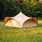 A boutique camping phoenix tent pitched in a grassy field with dense green trees in the background