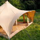 A boutique camping phoenix bell tent pitched outdoors on green grass with trees in the background. The tent has a spacious open interior and mesh side panels.