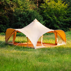 A boutique camping phoenix tent pitched on green grass with a dense forest in the background.