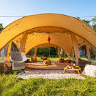 boutique camping phoenix tent set up outdoors in a grassy field under a blue sky, furnished with a chair, blanket, pillows, and a small table.