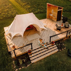 An aerial view of a luxury glamping setup featuring a boutique camping star emperor bell tent on a wooden deck, a small wooden cabin with a bathroom, and a couple sitting on the deck steps in the warm glow of sunset.