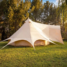 A boutique camping star emperor bell tent pitched on a grassy lawn with trees in the background, showing the tent's spacious design and open front.