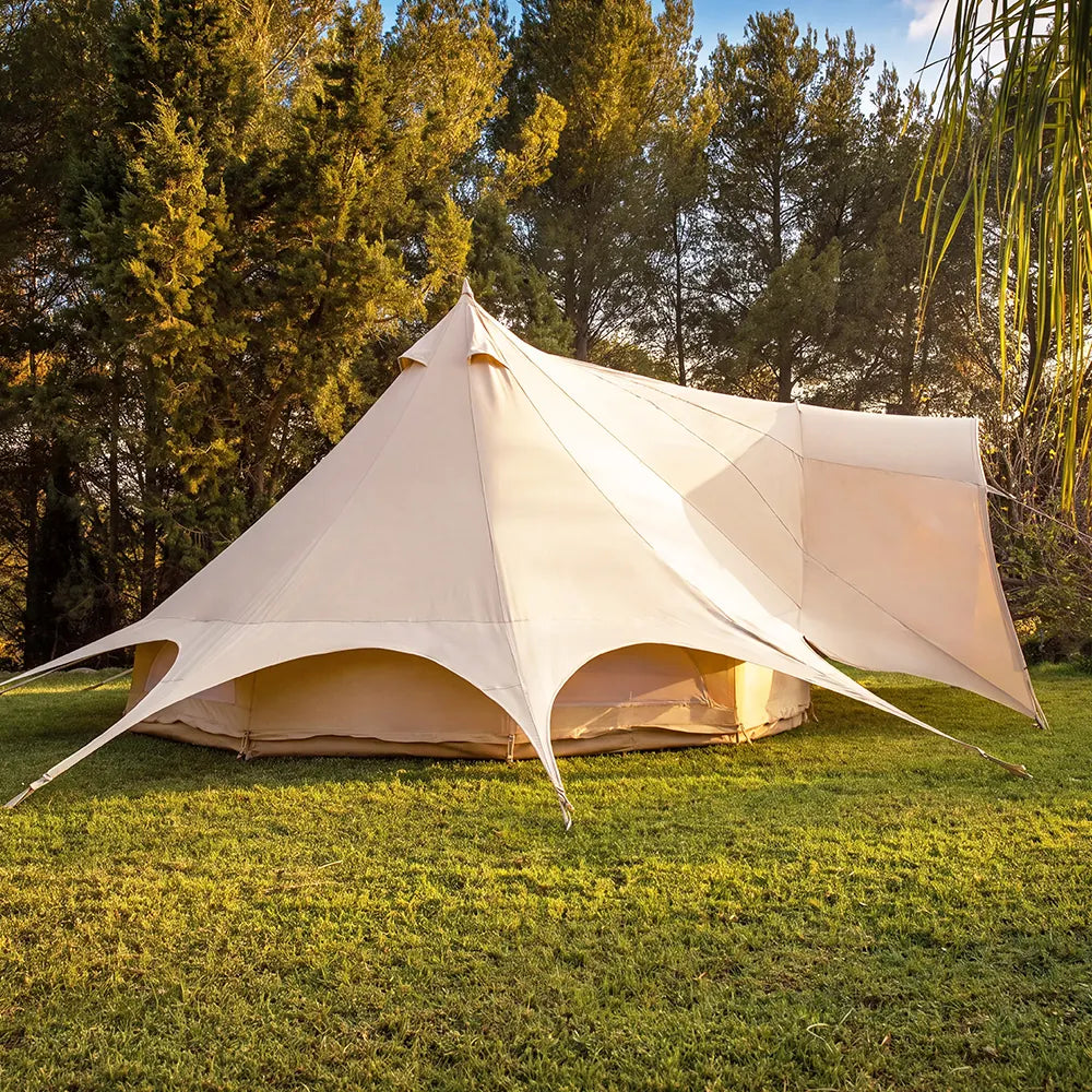 A boutique camping star emperor bell tent pitched on a grassy lawn with trees in the background, showing the tent's spacious design and open front.