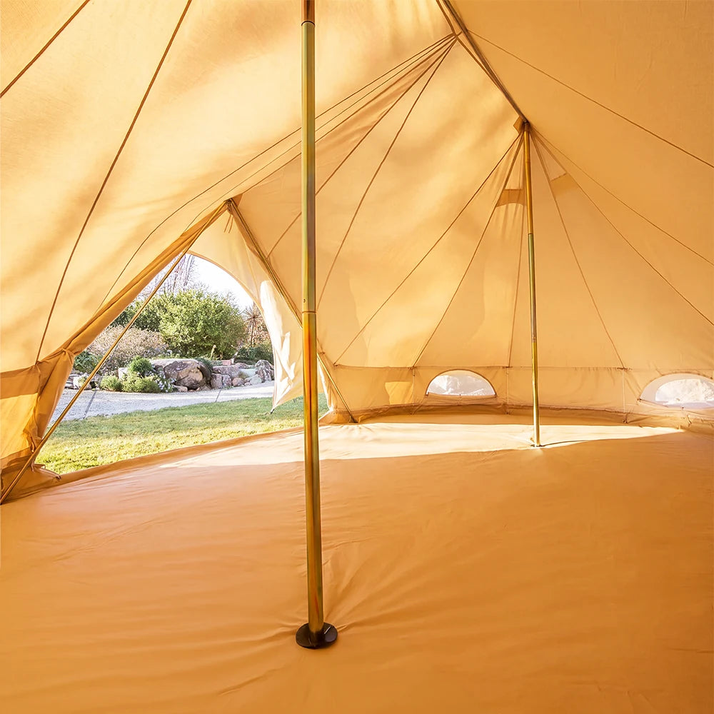Interior view of a boutique camping star emperor bell tent with a central pole and small window openings, with outdoor greenery visible through the side opening.