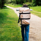girl walking carrying a boutique camping bell tent on a boutique camping backpack down a grassy forest pathway 