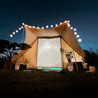 the boutique camping tucana tent glowing brightly in front of a deep blue night sky with fairy lights and plants dotted around the tent