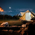 the tucana tent under a night sky featuring a dog laying down in the foreground infront of some cobbled steps with the moon in the background